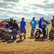 Riders and spectators standing and talking beside a row of parked bikes.