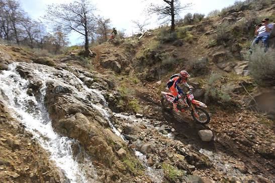 Riders working through the rock section of the Honey Lake track while spectators watch from the bank above.